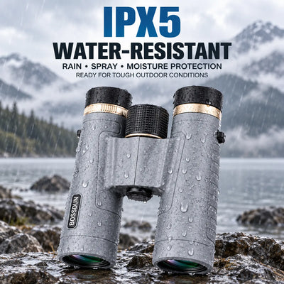 Gray BOSSUN binoculars with black and gold accents, shown outdoors on wet rocks with rain, water droplets, and misty mountains in the background. Text at the top reads 'IPX5 WATER-RESISTANT' with smaller copy about rain, spray, and moisture protection.
